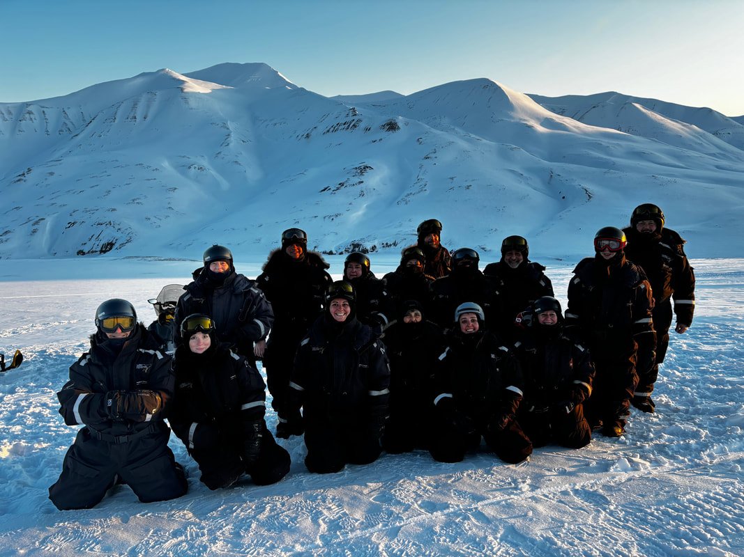 Gruppo di persone vestite da neve in posa sulla neve con montagne innevate sullo sfondo alle Isole Svalbard.