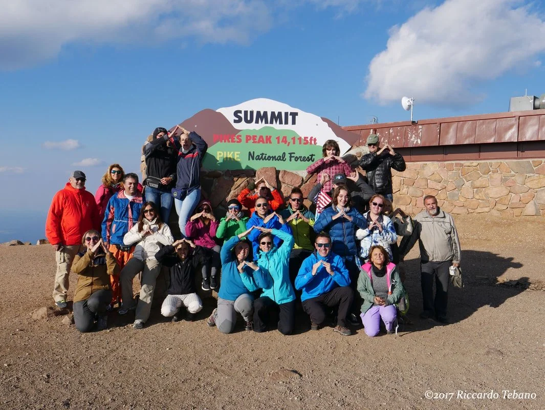 Gruppo di escursionisti alla vetta di Pikes Peak in Colorado Stati Uniti d'America con pannello che indica il nome e l'altitudine del monte. Cielo sereno e nuvole sparse nel cielo.