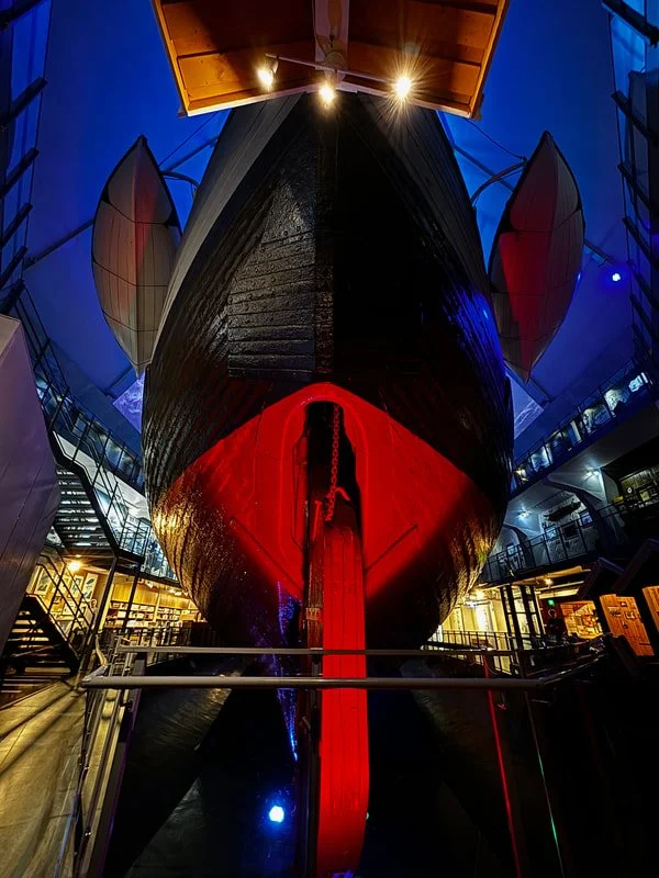 Nave Fram esposto nell'omonio museo a Oslo, visibile dalla prua occhiuta e dal timone rosso, con luci misteriose intorno.