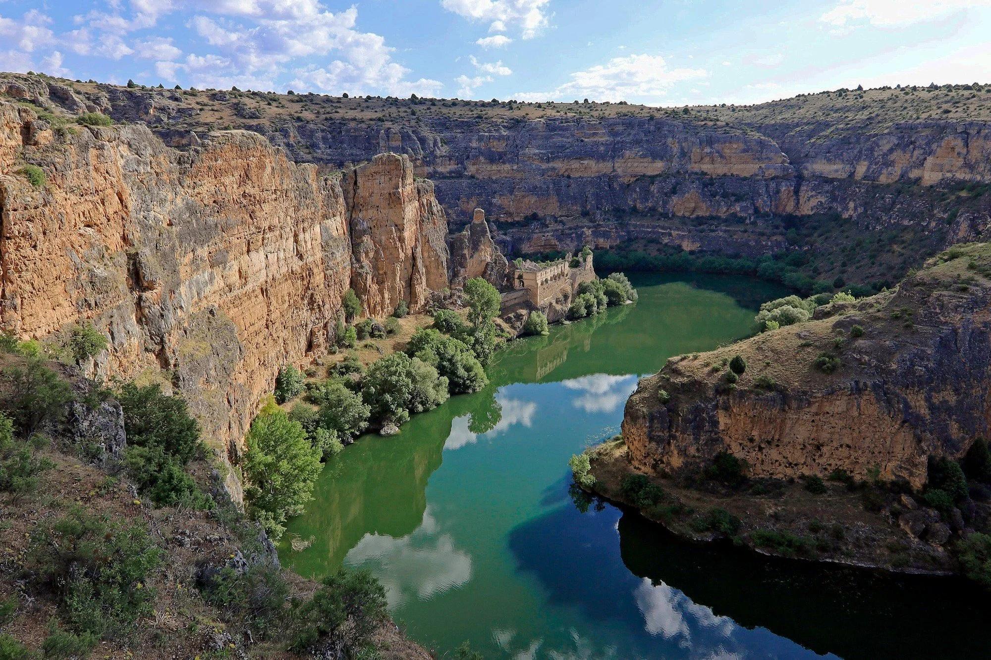 Vista di un canyon con pareti rocciose e un fiume verde con tutte e due le sponde ricoperte di vegetazione.