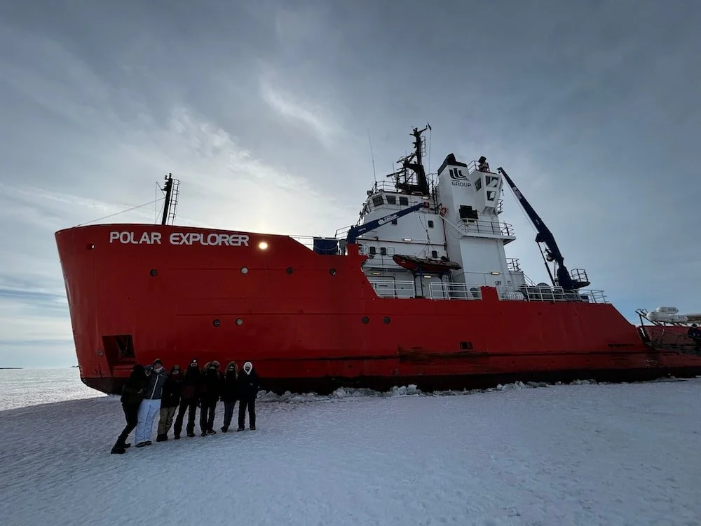 Gruppo di persone davanti a una grande nave rossa chiamata Polar Explorer sulla superficie ghiacciata del Golfo di Botnia in Svezia.