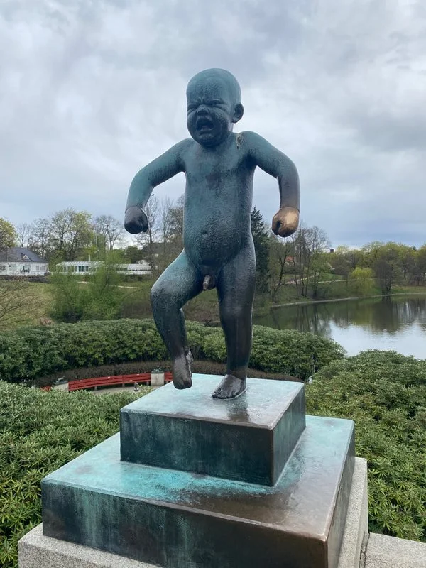 Statua di un bambino in piedi con il viso che urla o piange, con braccia flesse e un piede sollevato, in posizione di camminata, parco Vigeland a Oslo.