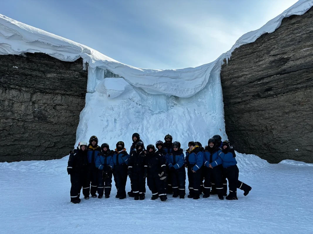 Gruppo di persone in abbigliamento invernale davanti a una cascata di ghiaccio in un paesaggio delle Isole Svalbard.