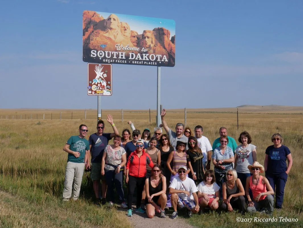 Gruppo di persone che posano davanti a un cartello di benvenuto a South Dakota con il Monte Rushmore sullo sfondo.