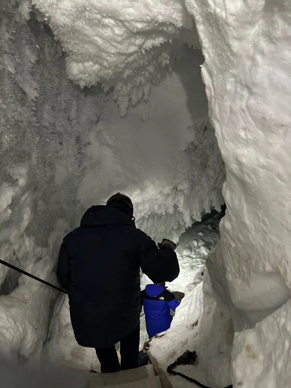 Due persone che attraversano un passaggio nella neve, circondate da alte pareti di ghiaccio in una grotta di ghiaccio, Longyearbyen, Isole Svalbard.