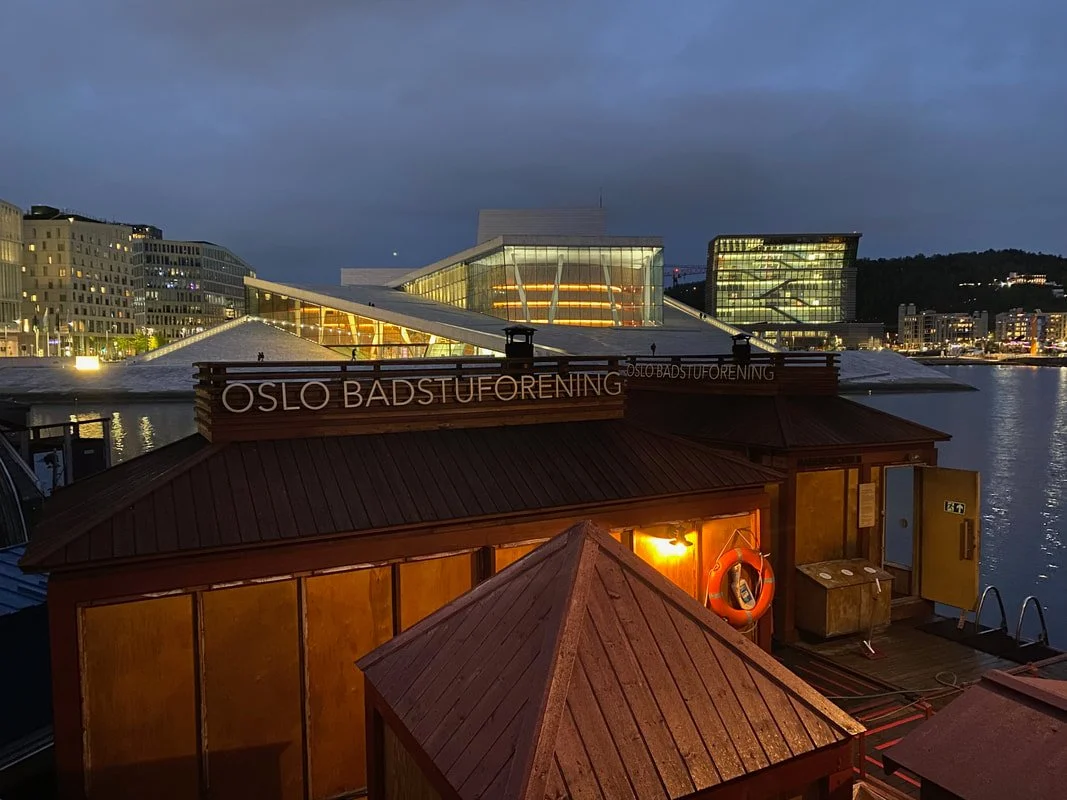 Veduta notturna di un edificio moderno vicino all'acqua con cartelli che dicono 'Oslo Badstuforening'.