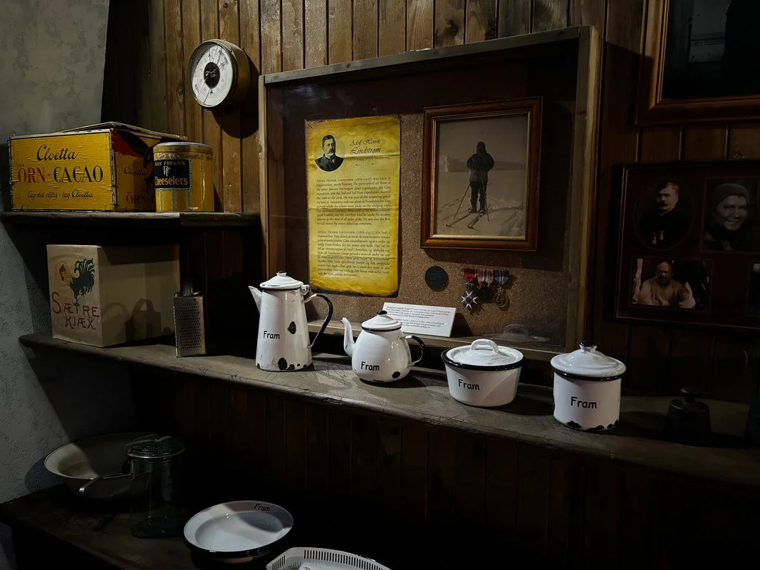 Decorazione di una vecchia parete con vari oggetti, foto storiche, medaglie e un orologio a muro, con alcuni contenitori e utensili sulla mensola in primo piano.