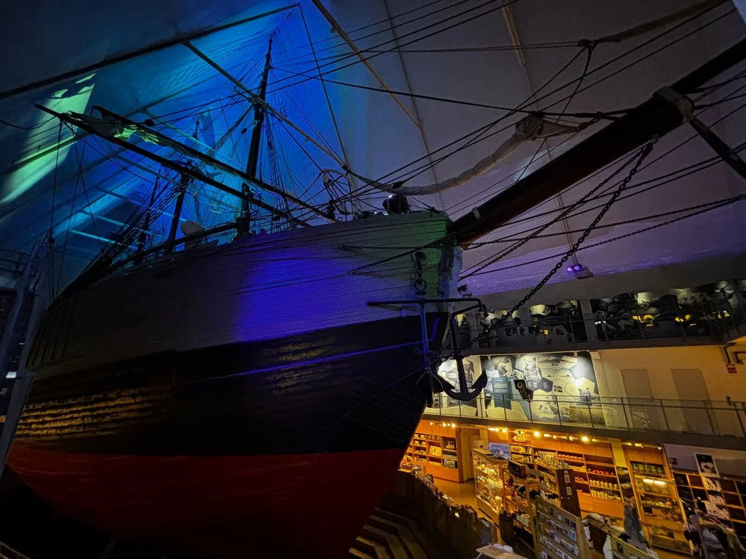 Museo Fram a Oslo in Norvegia con la grande nave storica esposta al interno, illuminata con luci multicolori, e un'area espositiva con oggetti e modelli navali.