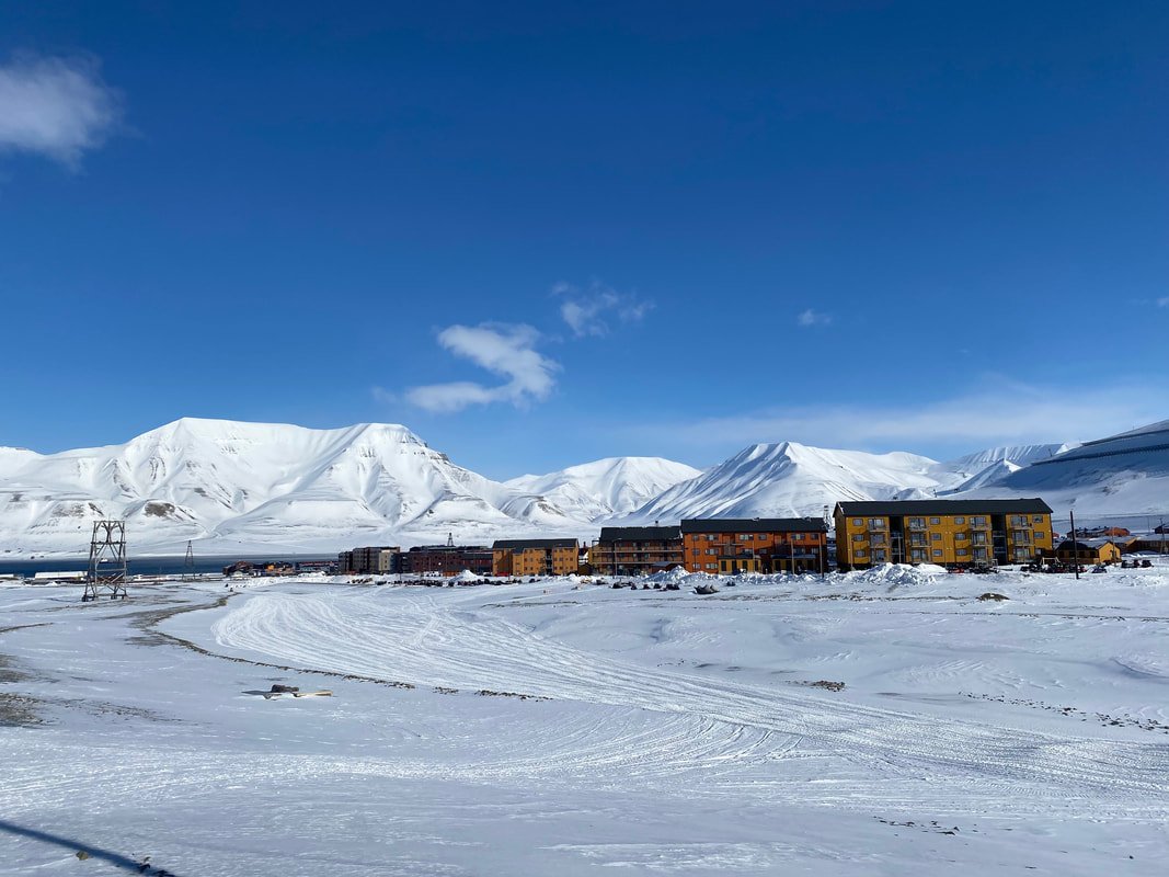 Paesaggio innevato con montagne innevate sullo sfondo, edifici colorati di fronte e cielo blu, Longyearbyen, Isole Svalbard.