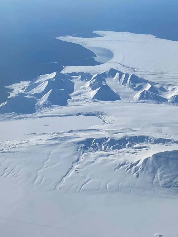 Veduta aerea di una regione ghiacciata con montagne di ghiaccio e neve alle Isole Svalbard, e un grande ghiacciaio che si apre verso il mare.