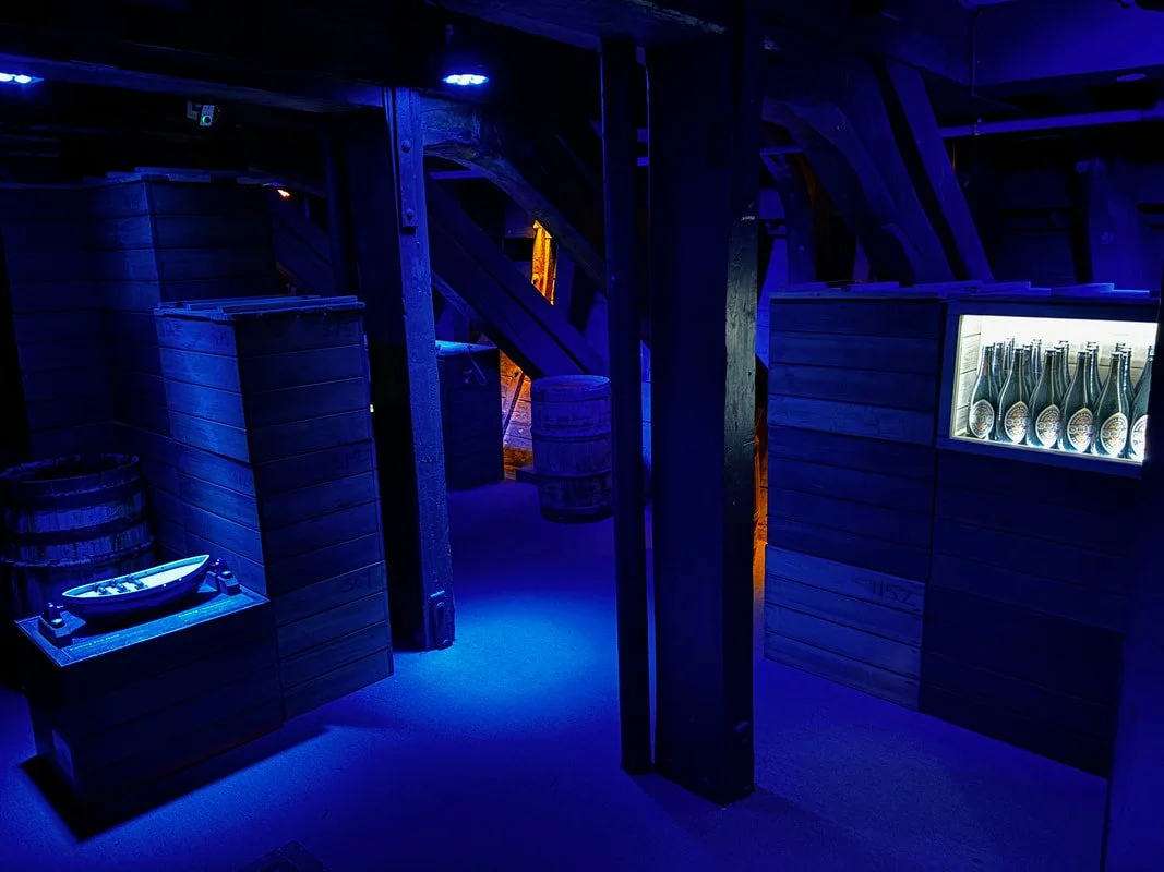 L'interno della cantina sotterranea della nave Fram con scaffali di bottiglie di vino e botti di legno, illuminata da luci blu
