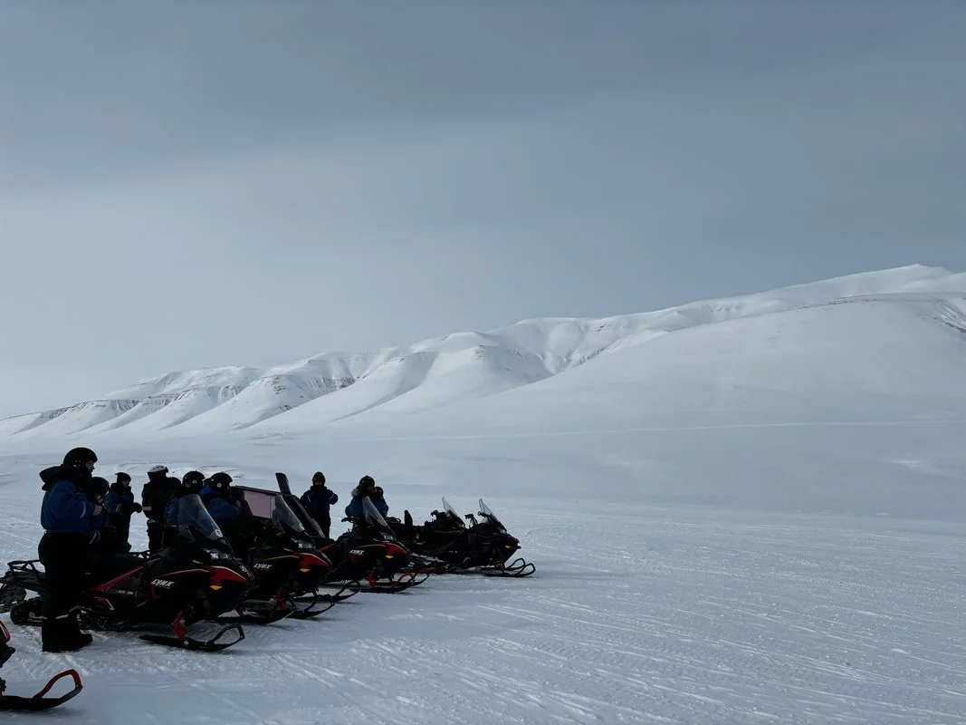 Gruppo di persone con motoslitte in un paesaggio innevato e montano, Isole Svalbard.