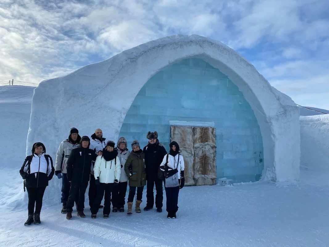 Gruppo di persone davanti all'entrata dell'Ice Hotel di Jukkasjärvi in Svezia sotto un cielo nuvoloso in un ambiente innevato.