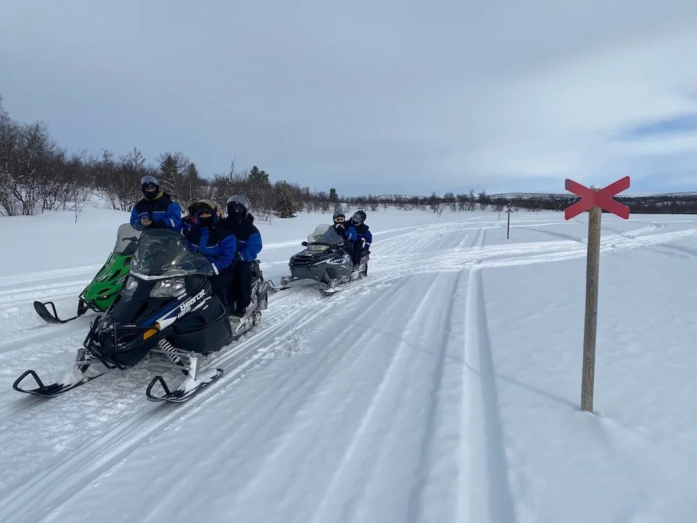 Gruppo di persone che guida motoslitte su un paesaggio innevato con cartello di attraversamento