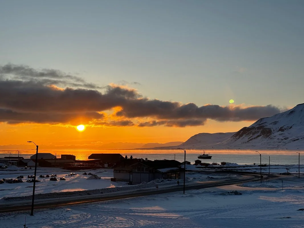 Tramonto su un paesaggio innevato con le montagne, il mare e alcune case, con una strada e lampioni, Longyearbyen, Isole Svalbard.