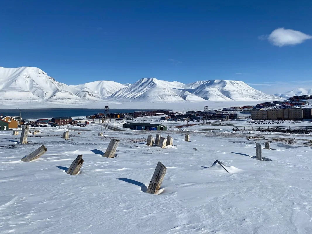 Paesaggio invernale con monti innevati, lago e case in una piccola città, sotto un cielo blu con alcune nuvole, a Longyearbyen, Isole Svalbard.