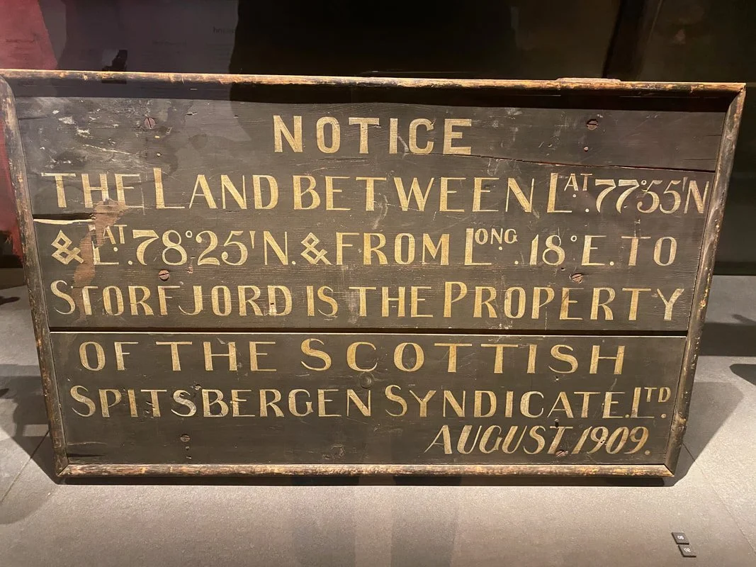 Avviso in legno vecchio con testo in inglese che indica i confini della terra tra le coordinate 77°55'S e 78°25'N, lungo 18° E, proprietà del sindacato scozzese di Spitsbergen, datato agosto 1909.