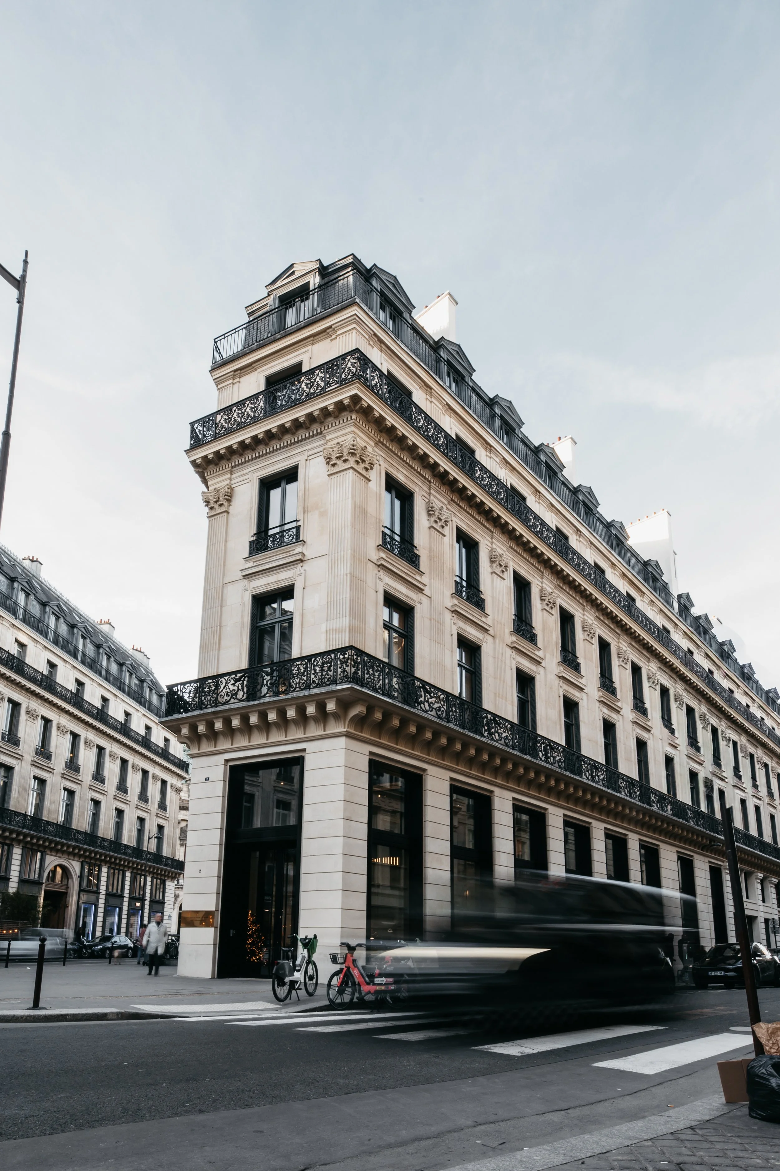 A tall, classical European-style building on a city street with bicycles and blurred vehicle motion in the foreground. photo made in Paris, architecture photography, by Canon 6D and sigma lens 11-24mm wide angle