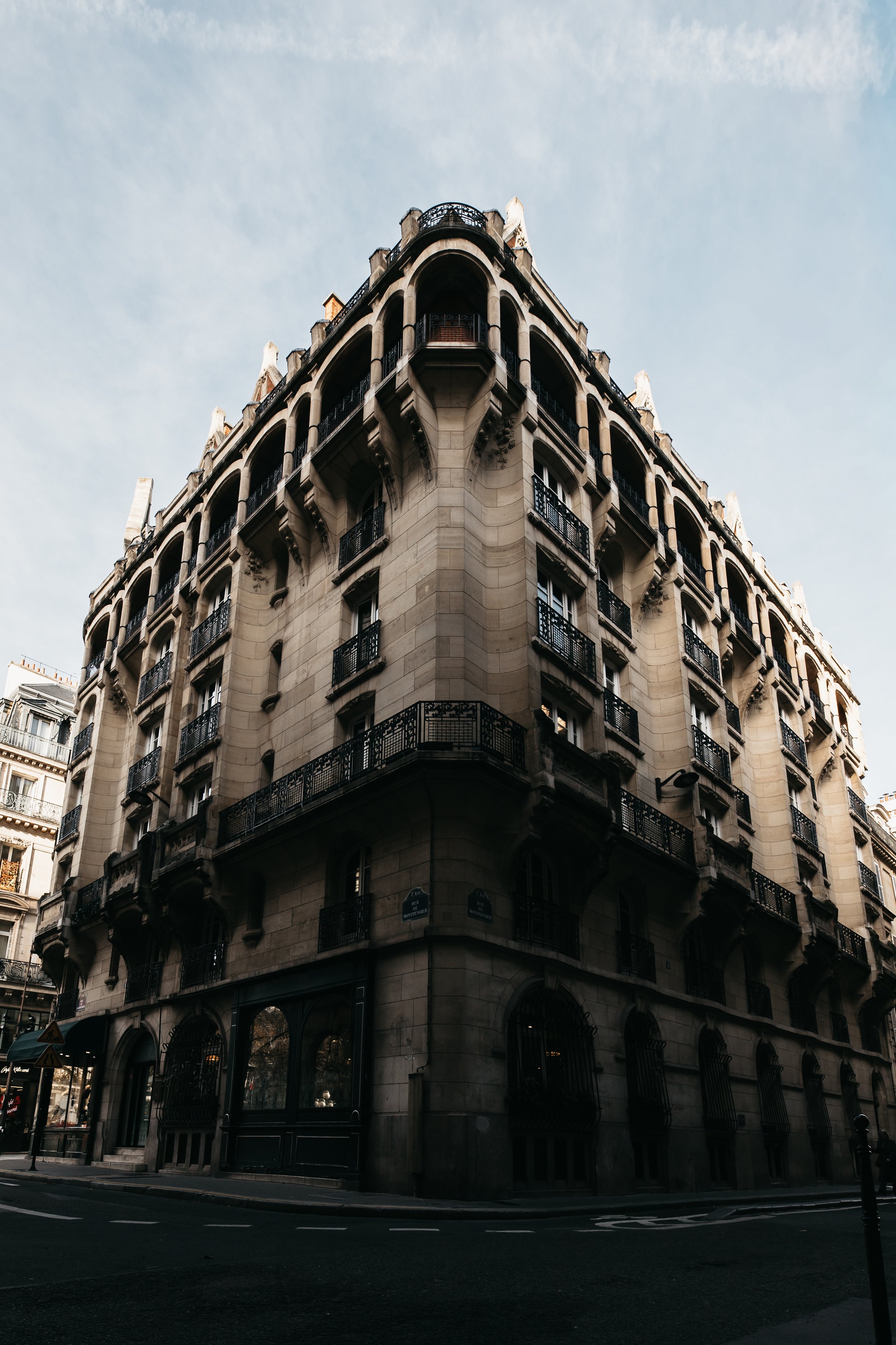 A historic Parisian building with classic stone architecture, arched windows, and ornate wrought-iron balconies, on a city street.