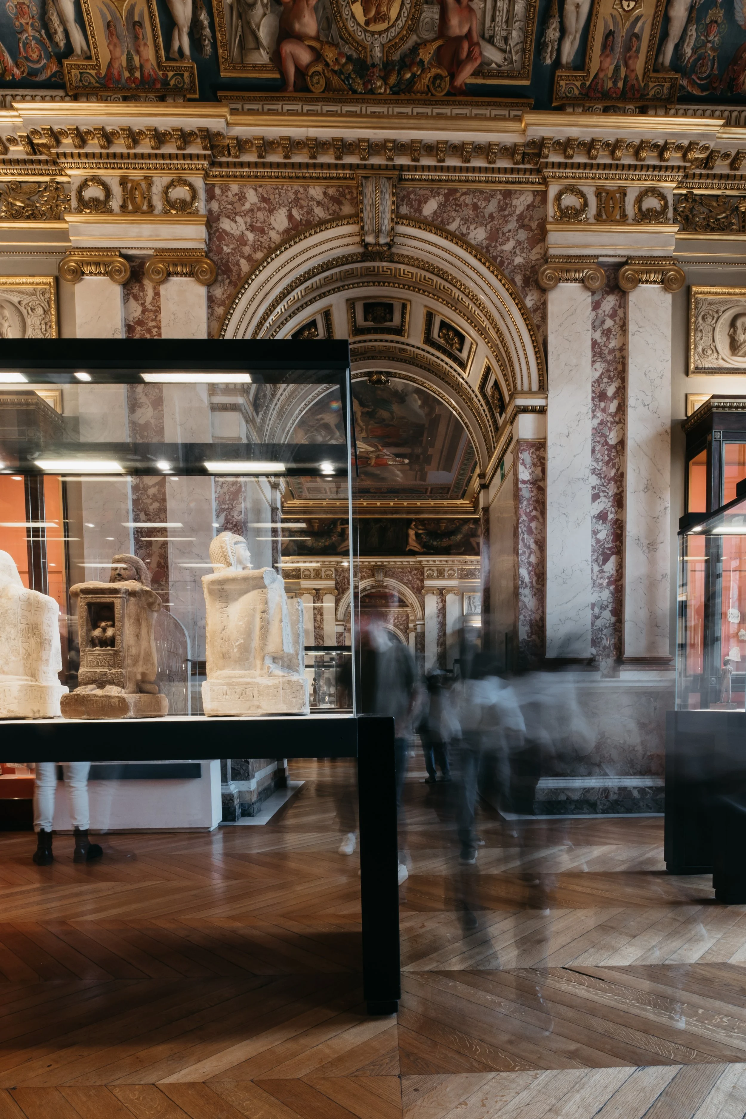Ancient Egyptian artifacts displayed in a museum with ornate gold and marble architecture and blurred visitors.
