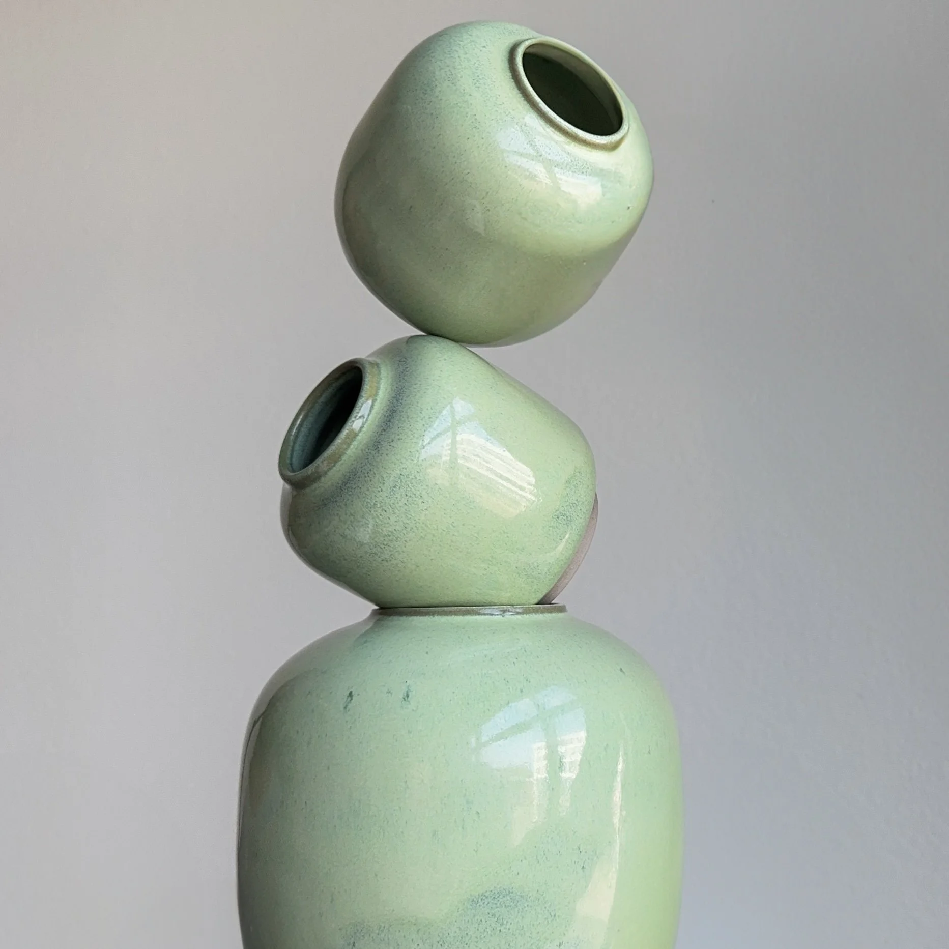 Three light green ceramic vases stacked vertically against a plain white background.
