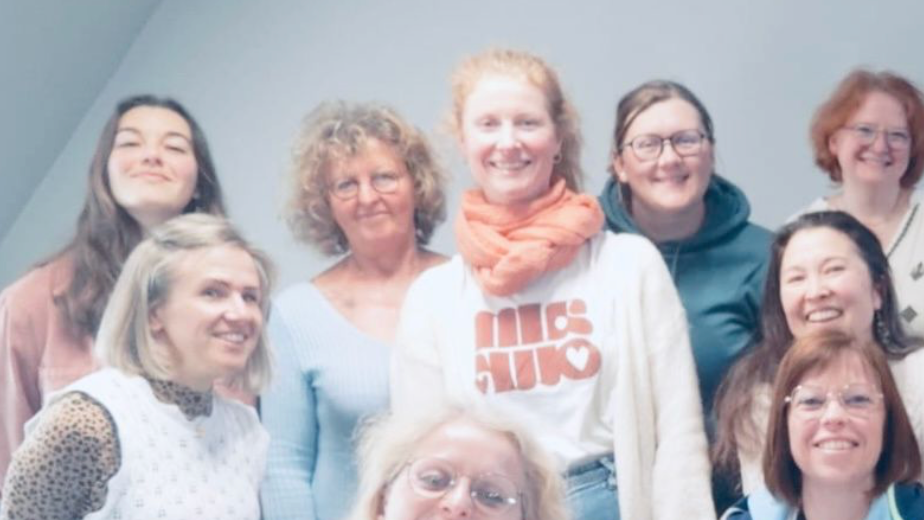 Groupe de neuf femmes souriantes posant pour une photo en intérieur.