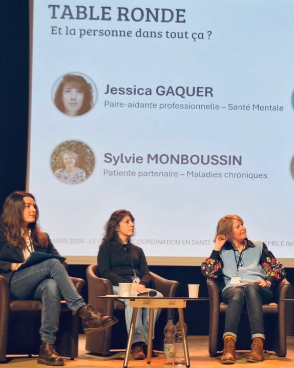 Présentation lors d'une table ronde avec trois femmes assises sur scène, affichage numérique en arrière-plan avec leurs noms et professions.
