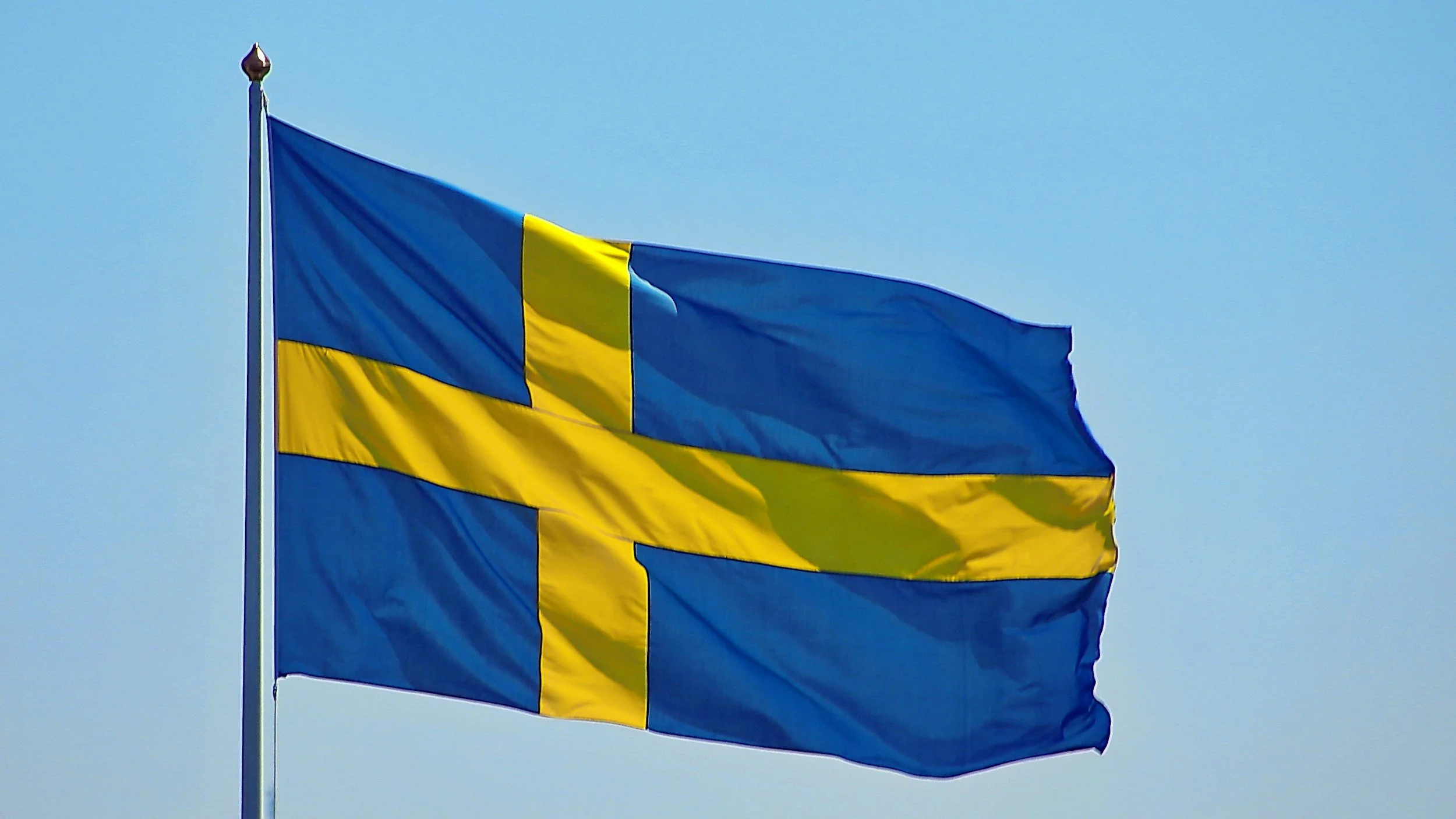 Two Swedish flags flying on a pole against a blue sky.