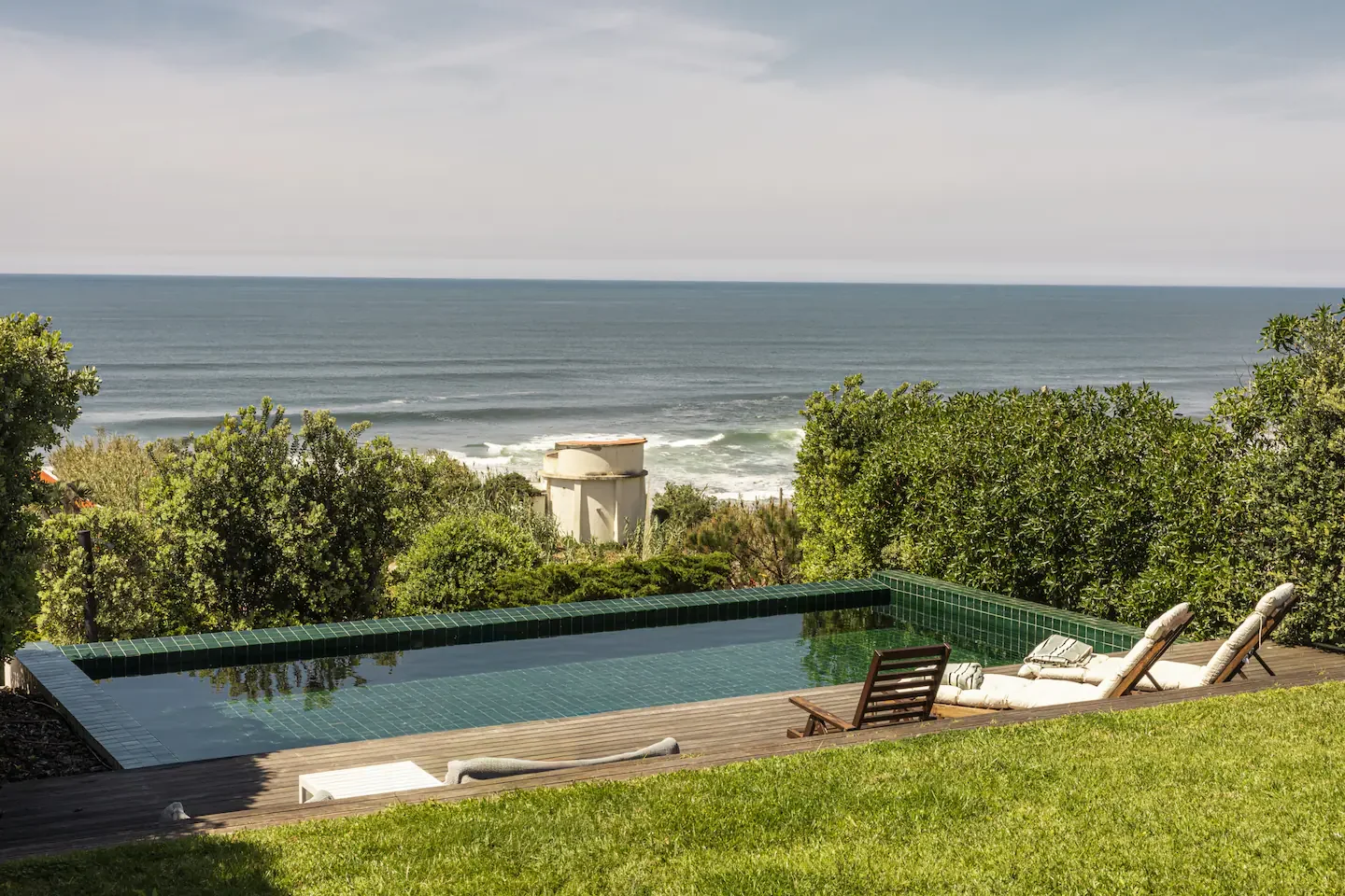 Swimming pool with lounge chairs overlooking the ocean, surrounded by greenery.