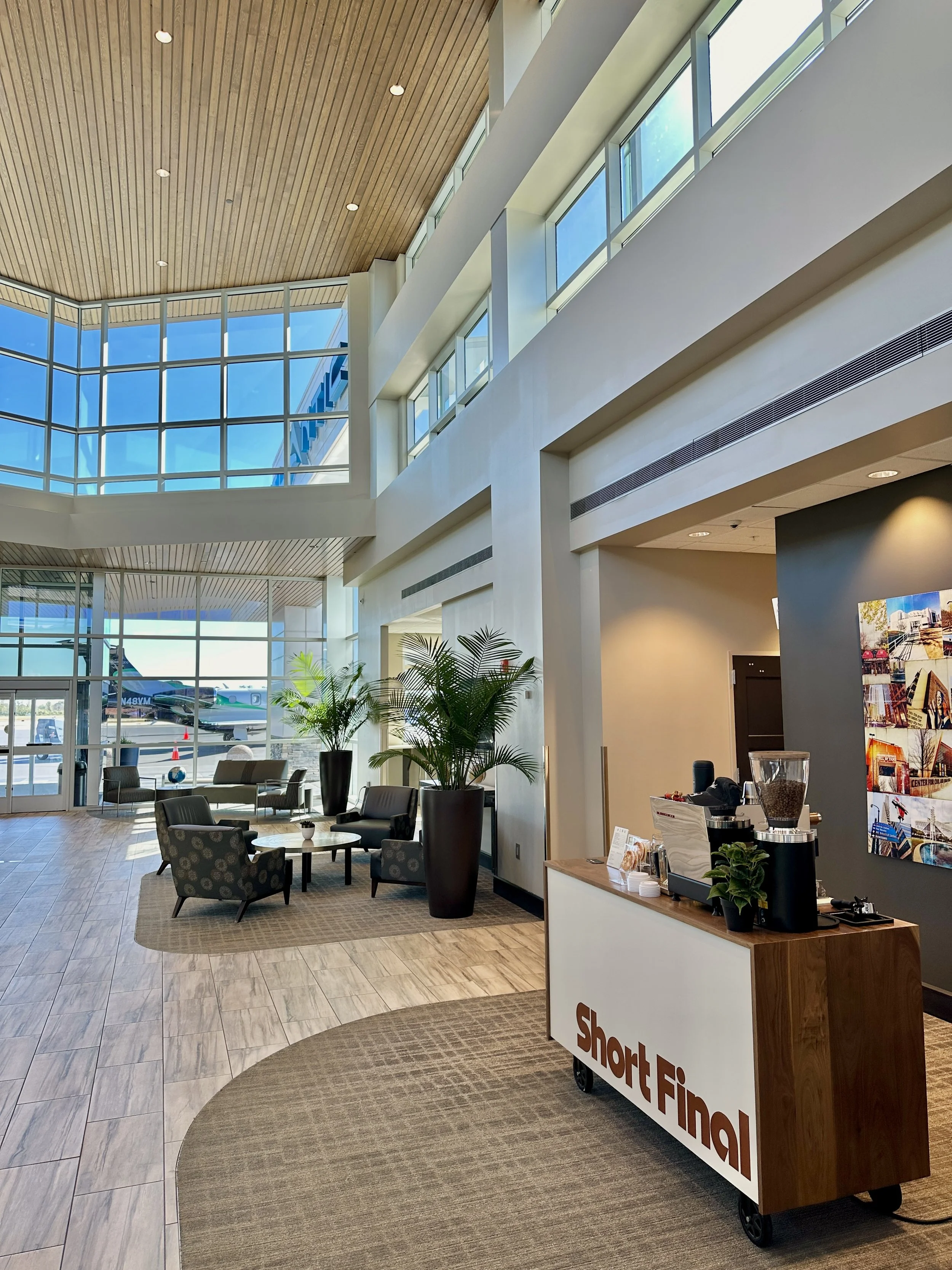 Modern airport terminal with seating area, large glass windows, and a baggage check-in counter labeled 'Short Final'.