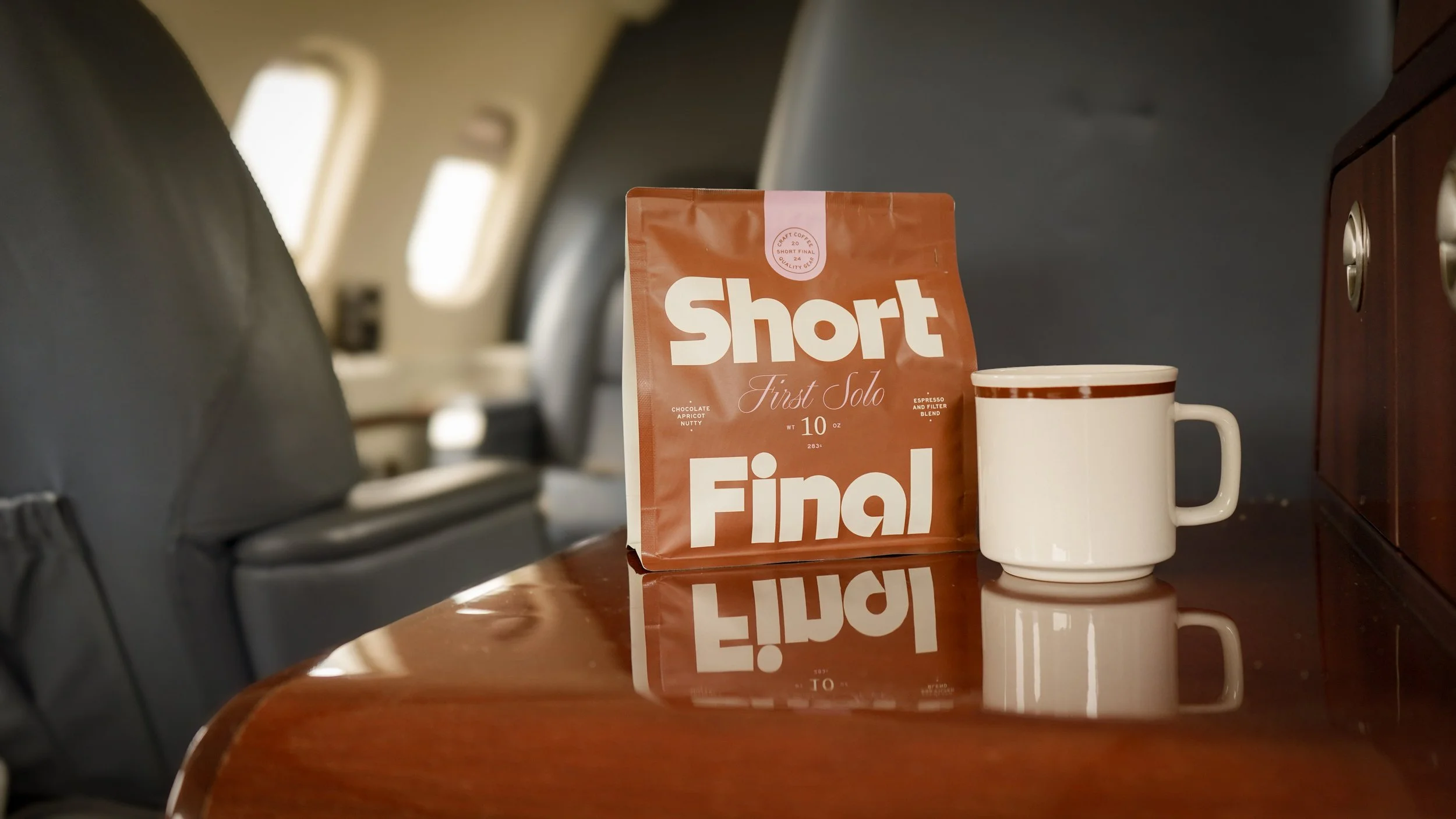 A package of Short Final coffee and a white mug with a brown rim on an airplane tray table.