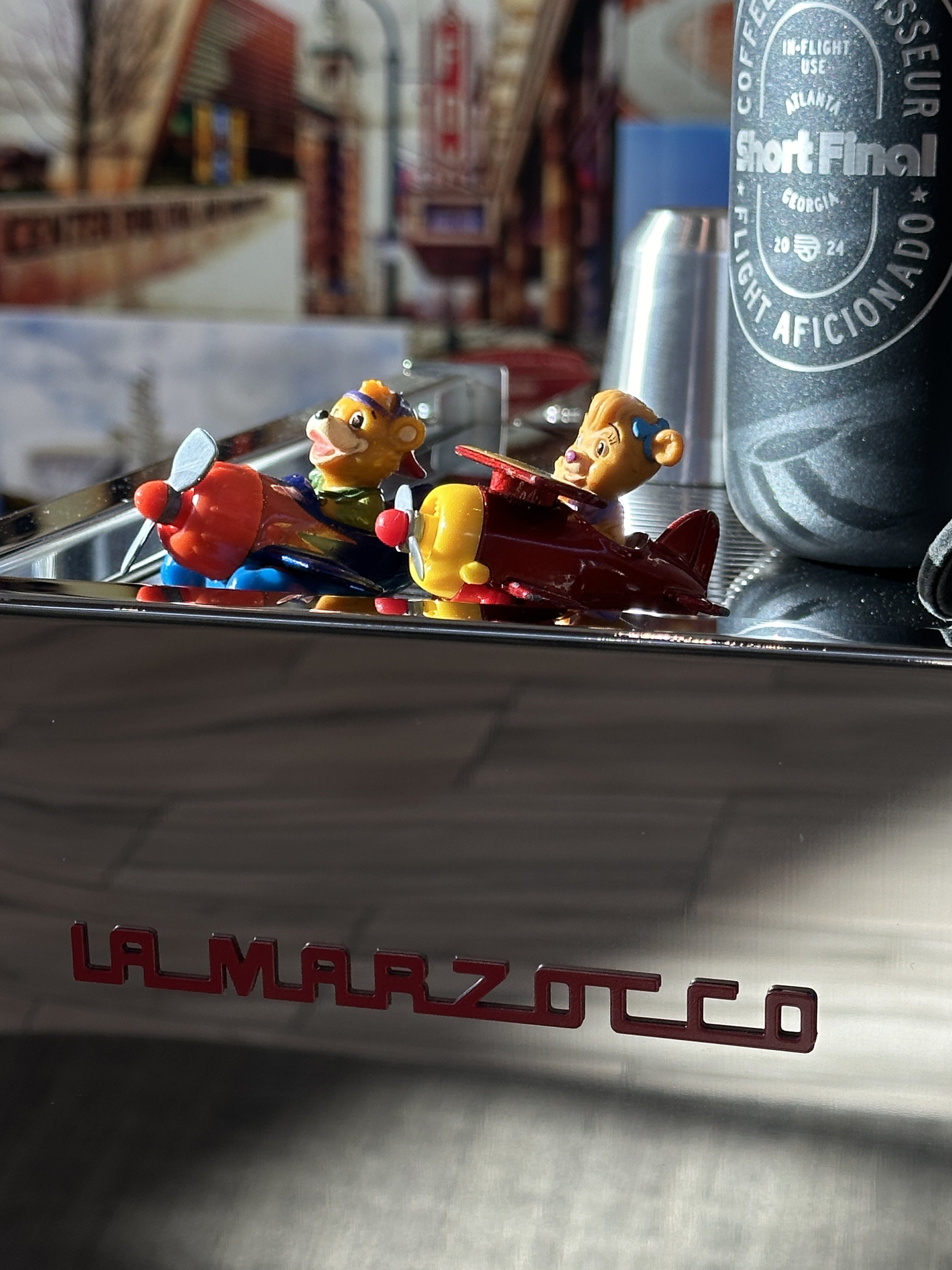 Close-up of a metallic LAMARZOCCO , Short Final gear, and a blurred background of a cafe or restaurant.