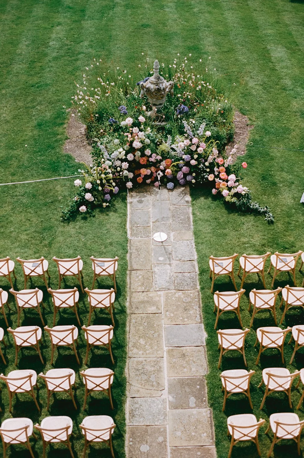 Outdoor wedding setup with rows of wooden chairs facing a flower-filled altar with a stone pathway.