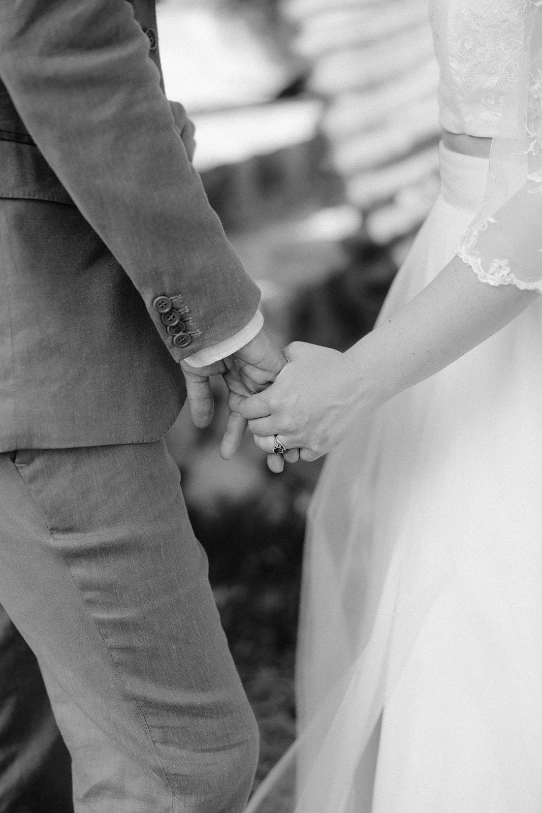 A couple holding hands during a wedding ceremony, with the bride wearing a white dress and wedding ring, and the groom wearing a suit.