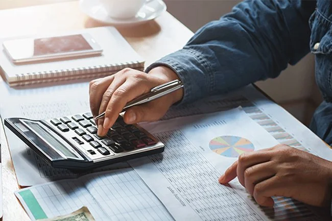 A person using a calculator while working on financial documents on a desk.