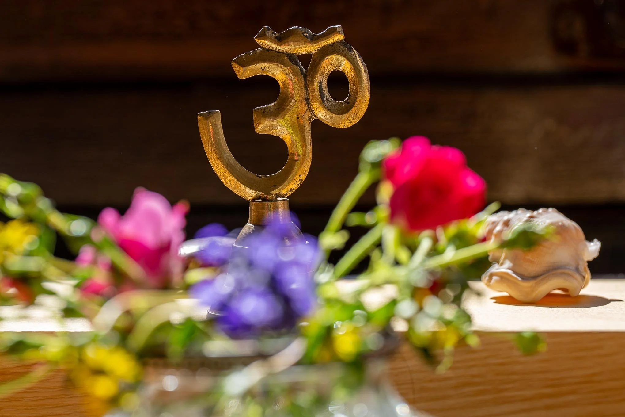 Göttin Ganesha symbol aus Metall auf Holzoberfläche, umgeben von bunten Blumen, im Sonnenlicht