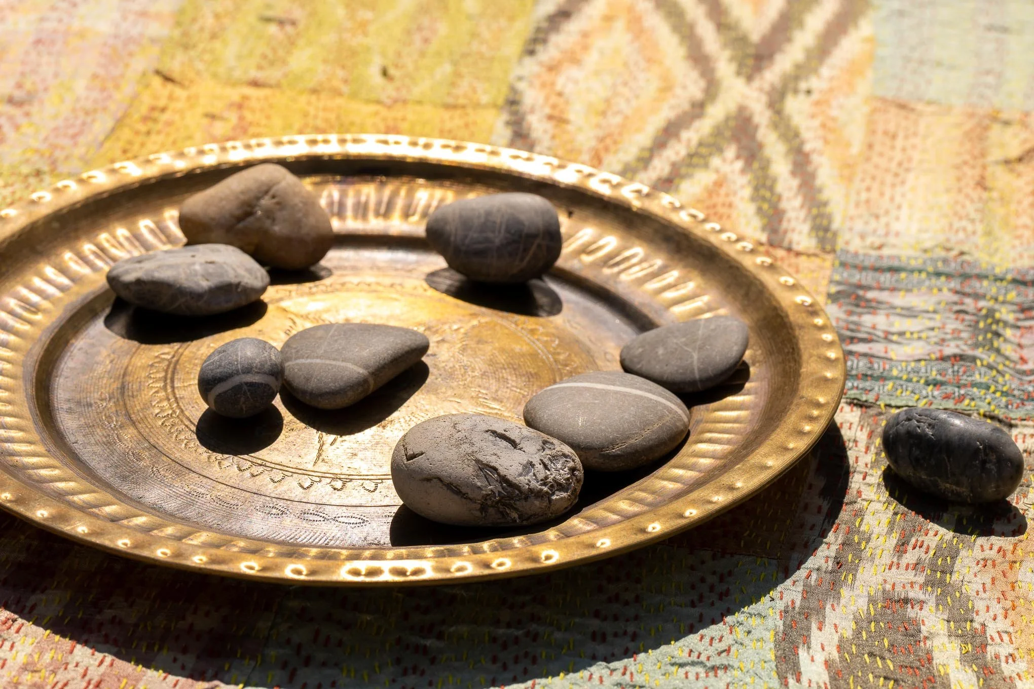 Eine goldene Schale mit glatten Steinen auf einem bunten Stoff.