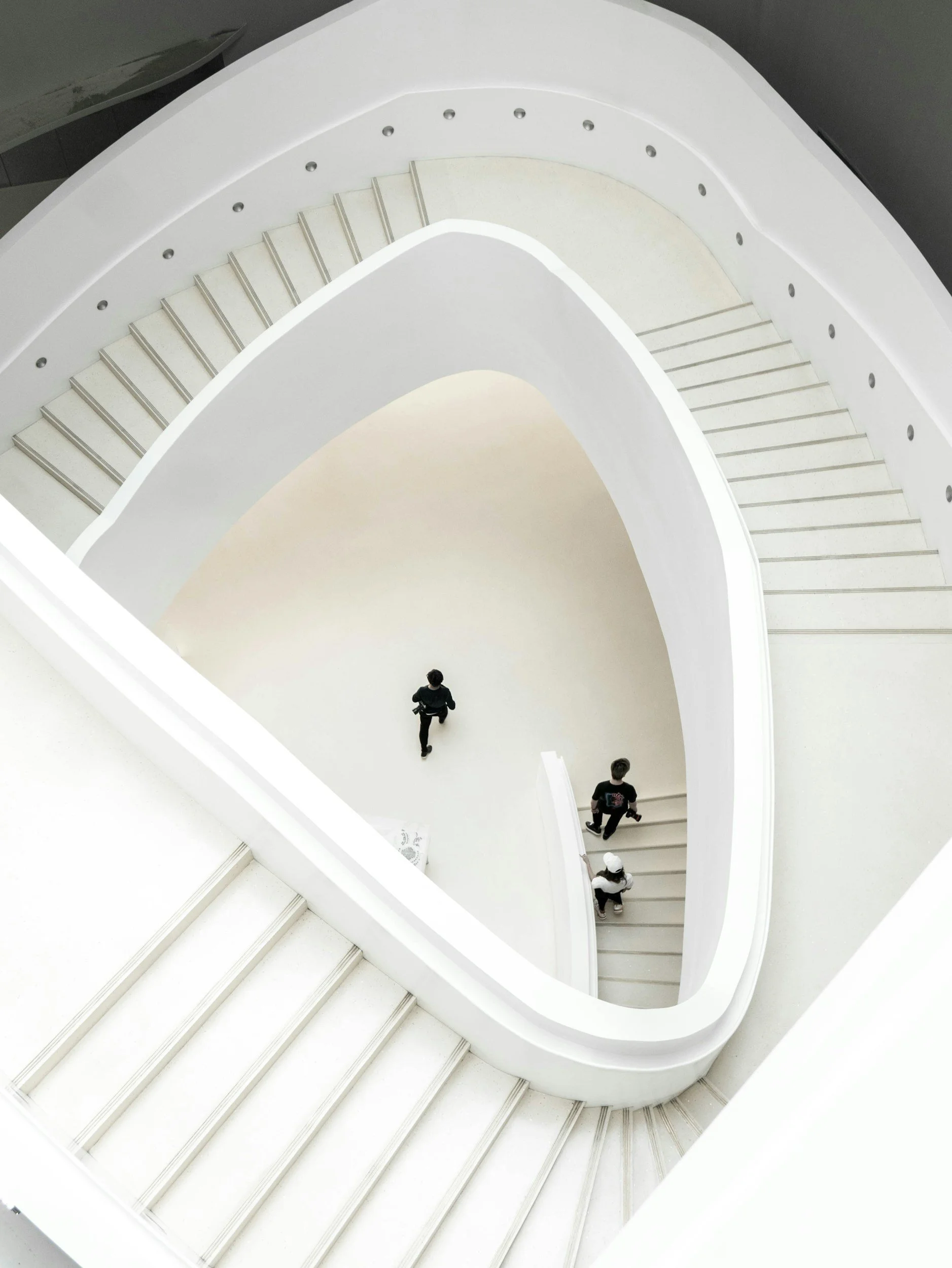Aerial view of a modern, white, spiral staircase with three people walking down it.