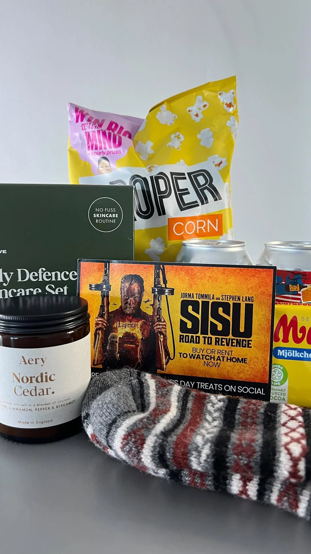 A collection of various items including a bag of popcorn, a skincare routine box, a chocolate spread jar, a movie rental flyer for 'Sisu,' two cans of soda, and a sock with a striped pattern.