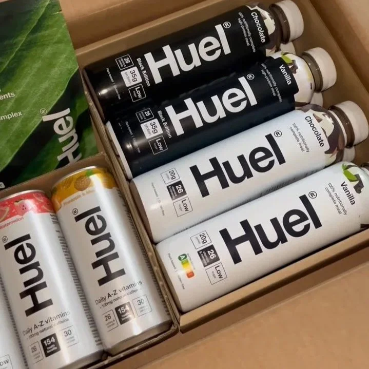 A variety of Huel meal replacement products, including bottles and cans, in different flavors and formulations, arranged in a box.