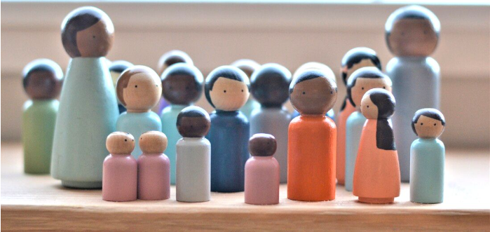 Collection of wooden figurines representing people, varying in size, color, and gender, arranged on a wooden surface.