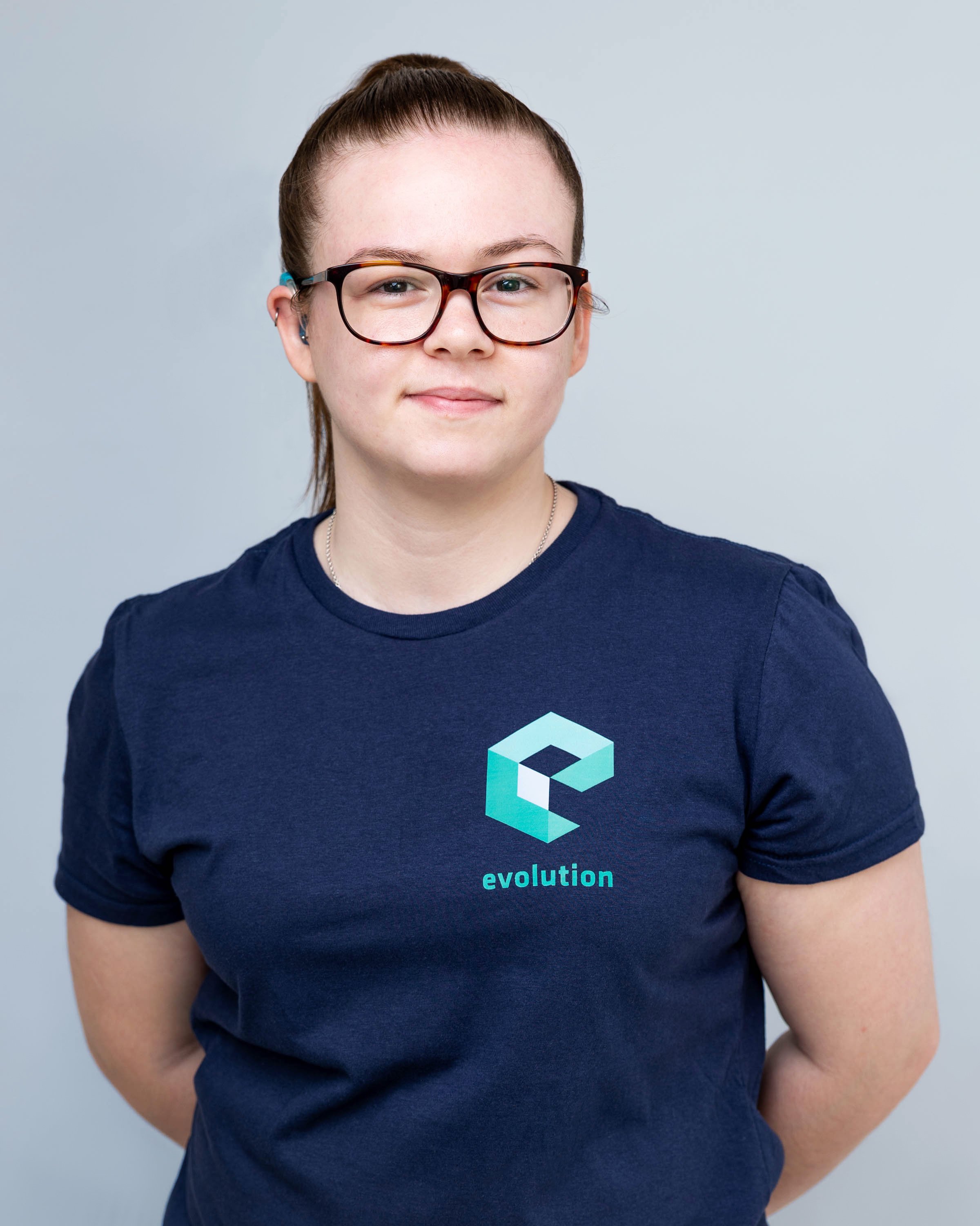 A person with glasses wearing a navy blue t-shirt with an abstract 'E' logo and the word 'evolution' on it, standing against a light gray background.