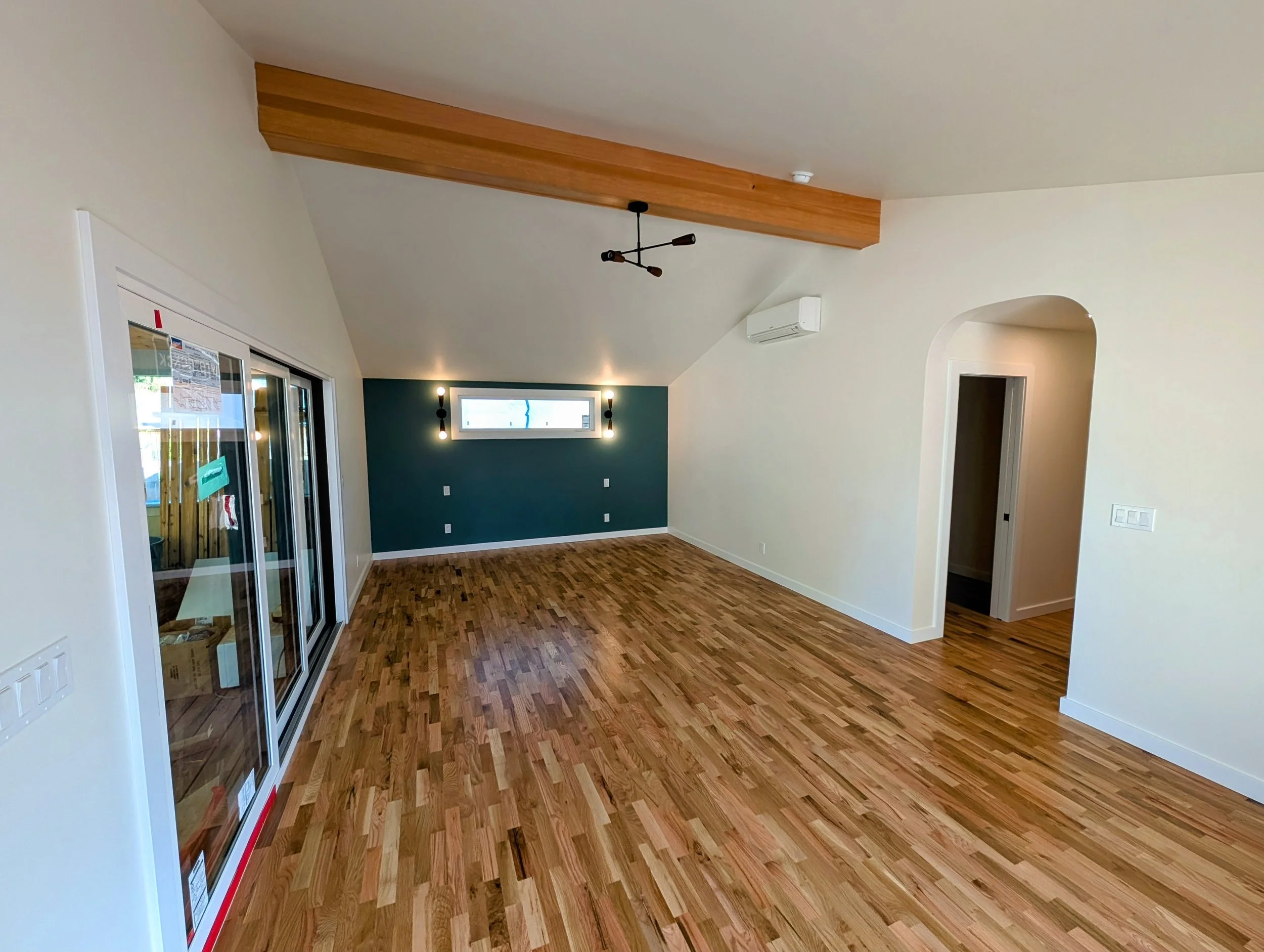 Empty living room with hardwood floors, a dark green accent wall, a small window, sliding glass door, and modern ceiling lighting.