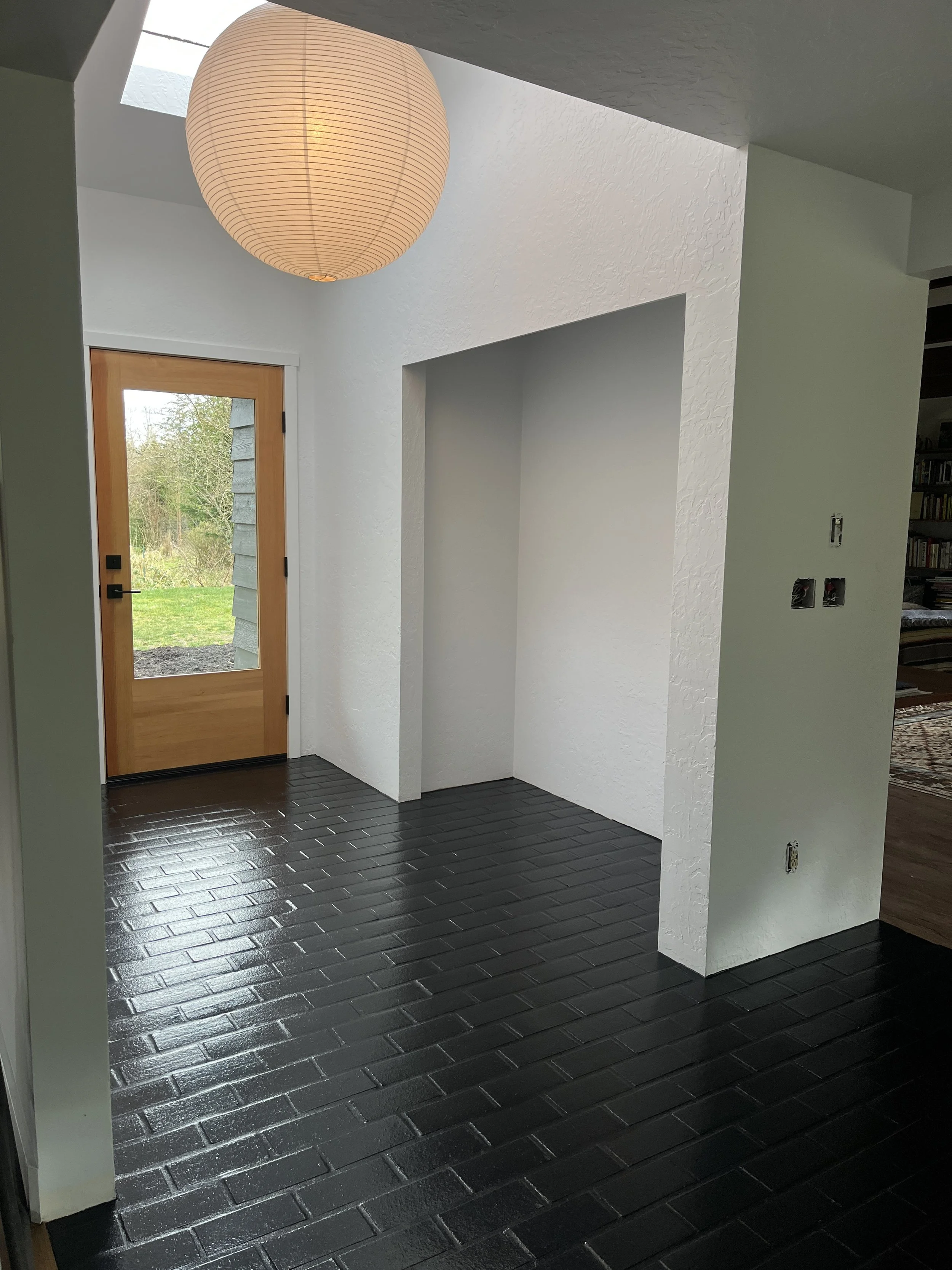 Entrance area with black tiled floor, wooden door with glass panel, white textured walls, and a large round paper lantern hanging from the ceiling.