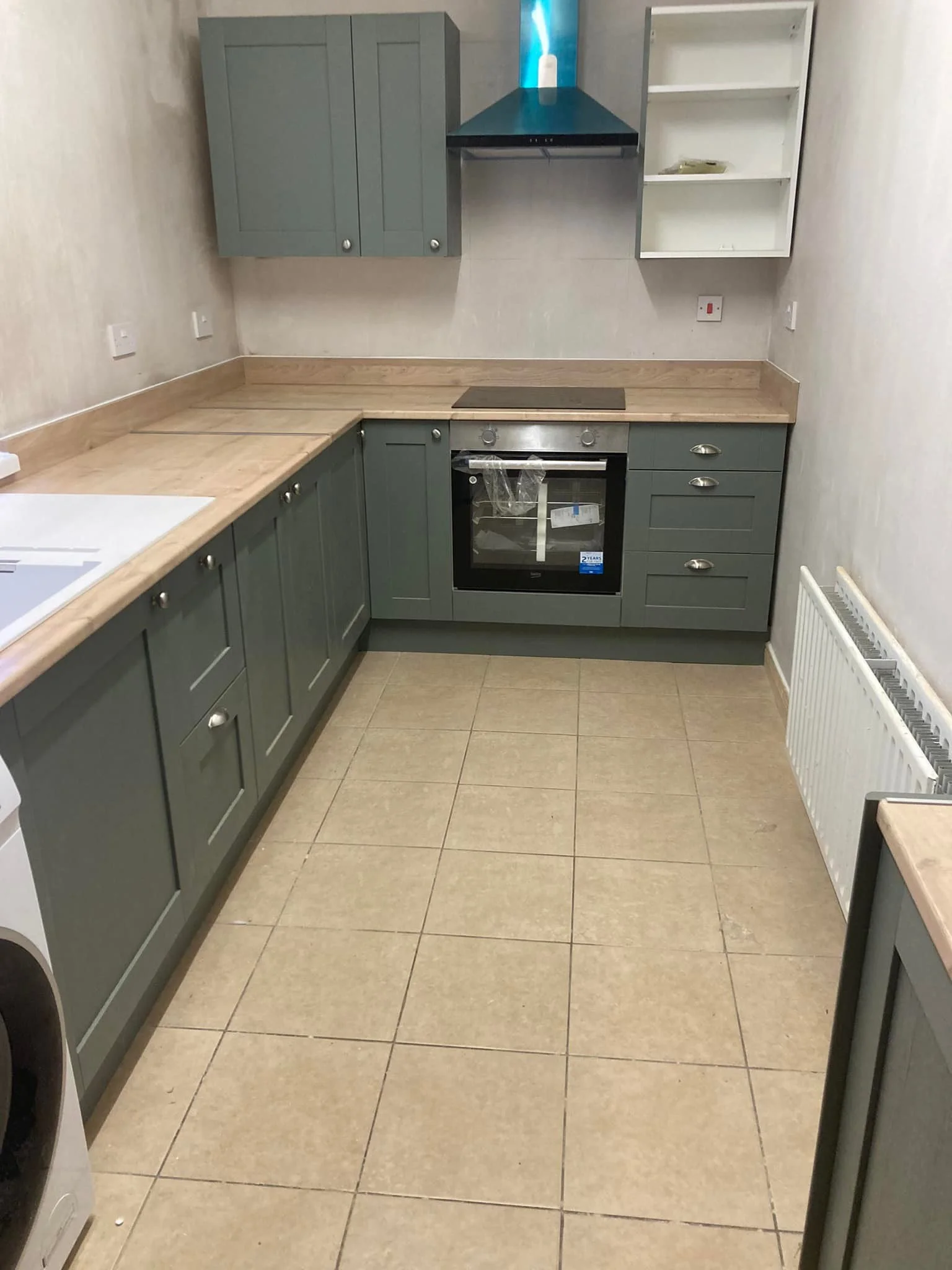Sage green fitted kitchen with integrated oven and extractor hood