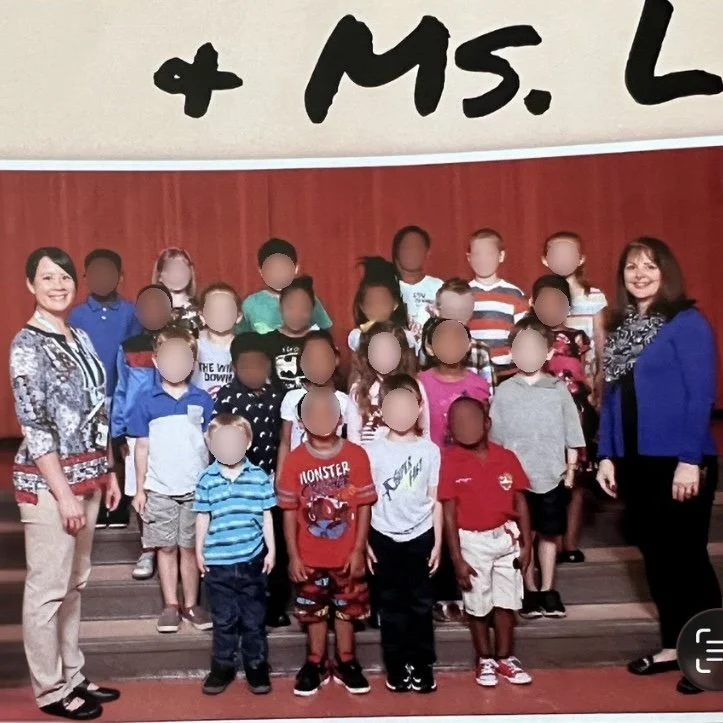Kindergarten class picture day: Group of young children and two teachers posing on a stage with a wooden background.