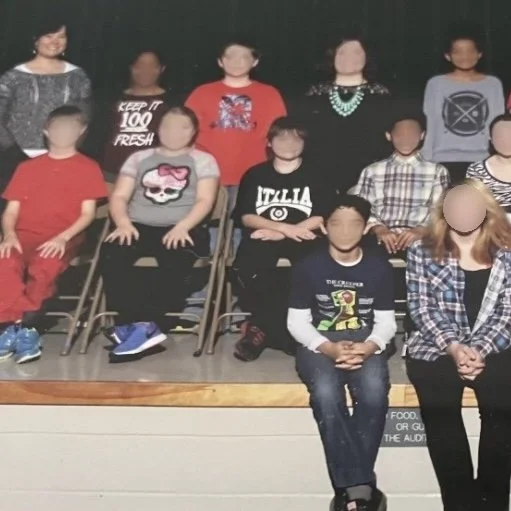 Ms. Lo's former 5th grade class: Group photo of elementary school children and a teacher in a classroom, with students seated and standing in rows on stage.