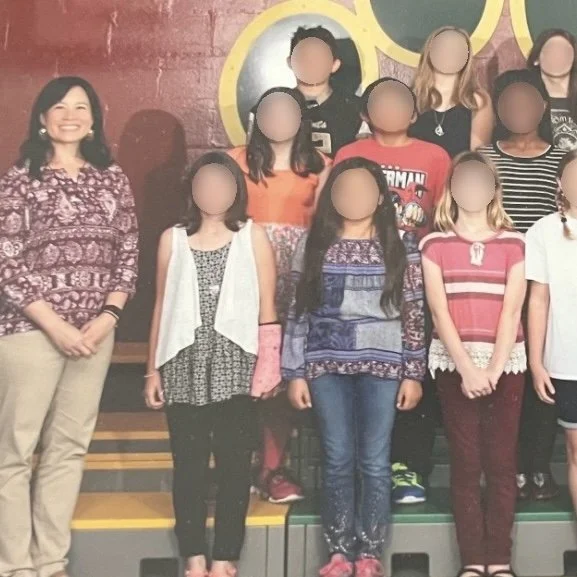 Ms. Lo's former 5th grade class: Group of elementary school students and a female teacher on a stage, smiling for a class photo.