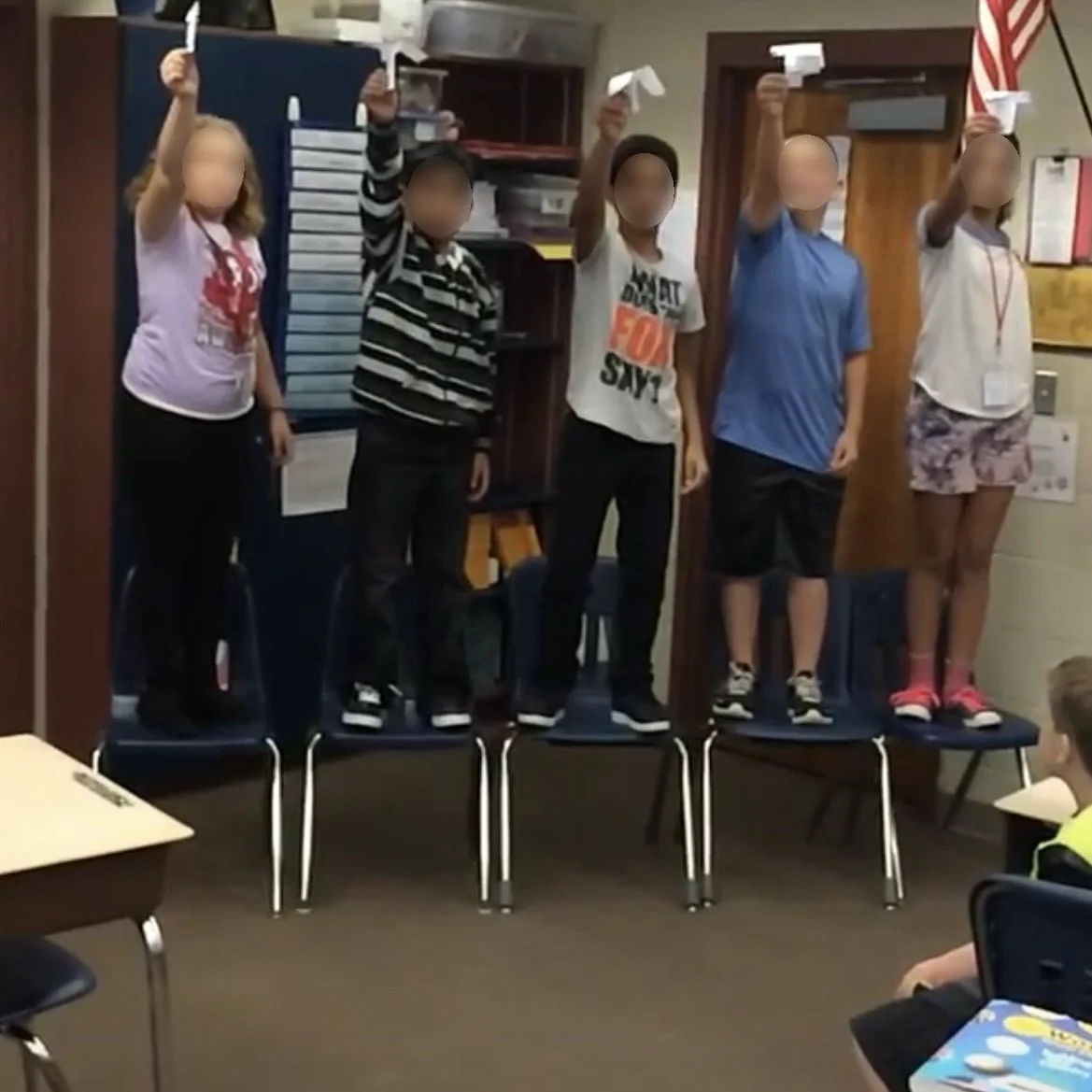 Ms. Lo's former 5th grade students participating in a Science Helicopter Lesson Activity she created: Five children standing on chairs, holding paper helicopters aloft, in a classroom.