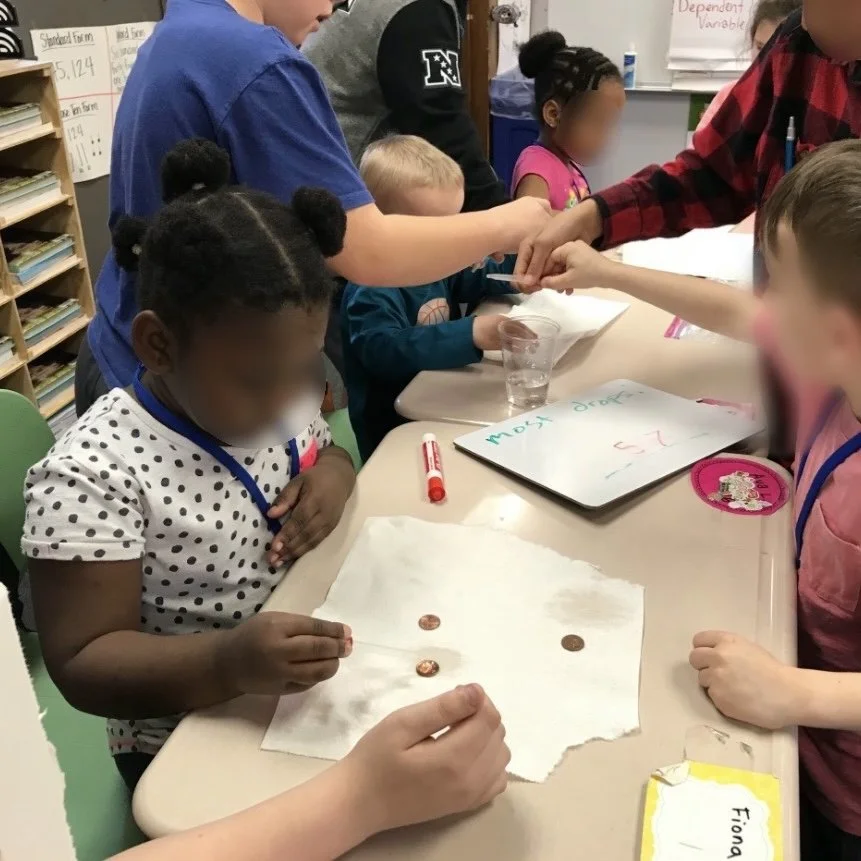 Children gathered around a table in a classroom, examining coins and engaging in a learning activity.